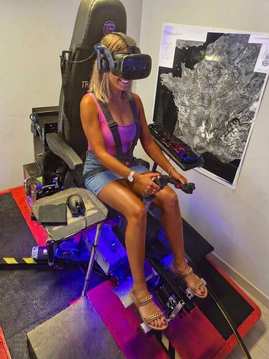 Une pilote aux commandes du simulateur d’hélicoptère HélicoSimu, casque de réalité virtuelle et harnais, devant la carte de France vue de satellite
